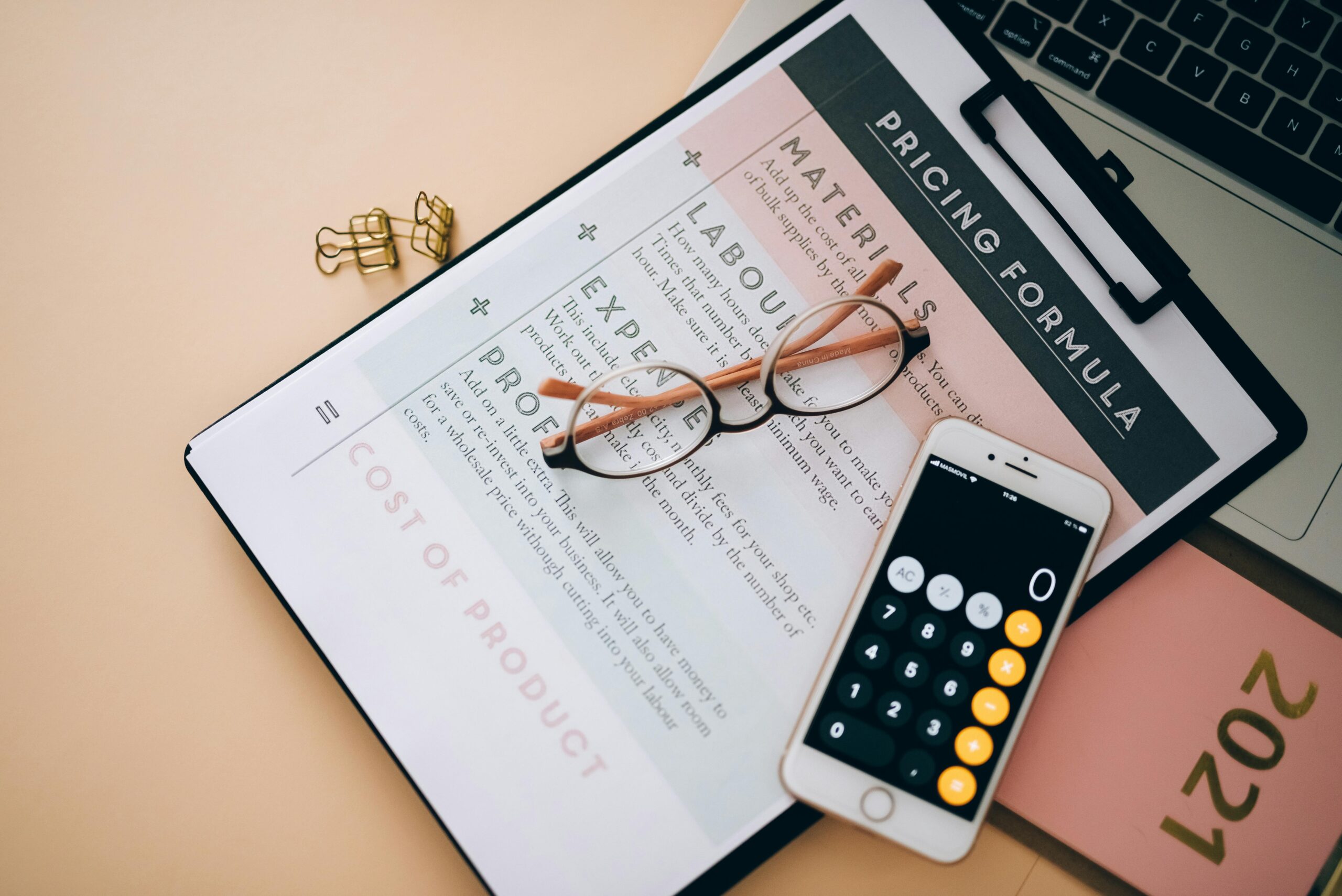 Desk flat lay with pricing formula worksheet, glasses, and calculator, representing financial planning and organization for 15 small business marketing apps.